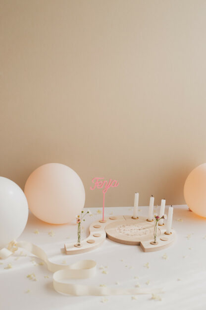 Auf diesem Bild sieht man einen Geburtstagskranz mit einem pinken Namens Stecker und Kerzen.